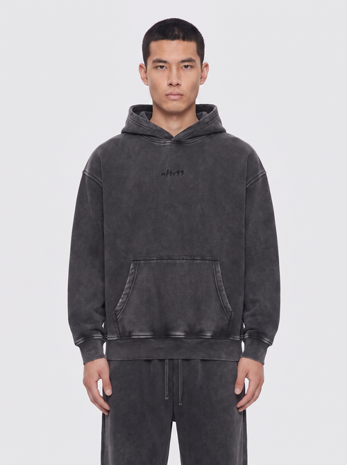 aftr99 | A man wearing a dark gray washed hoodie with a small black embroidered logo on the chest, paired with matching dark gray sweatpants, against a light gray studio background.